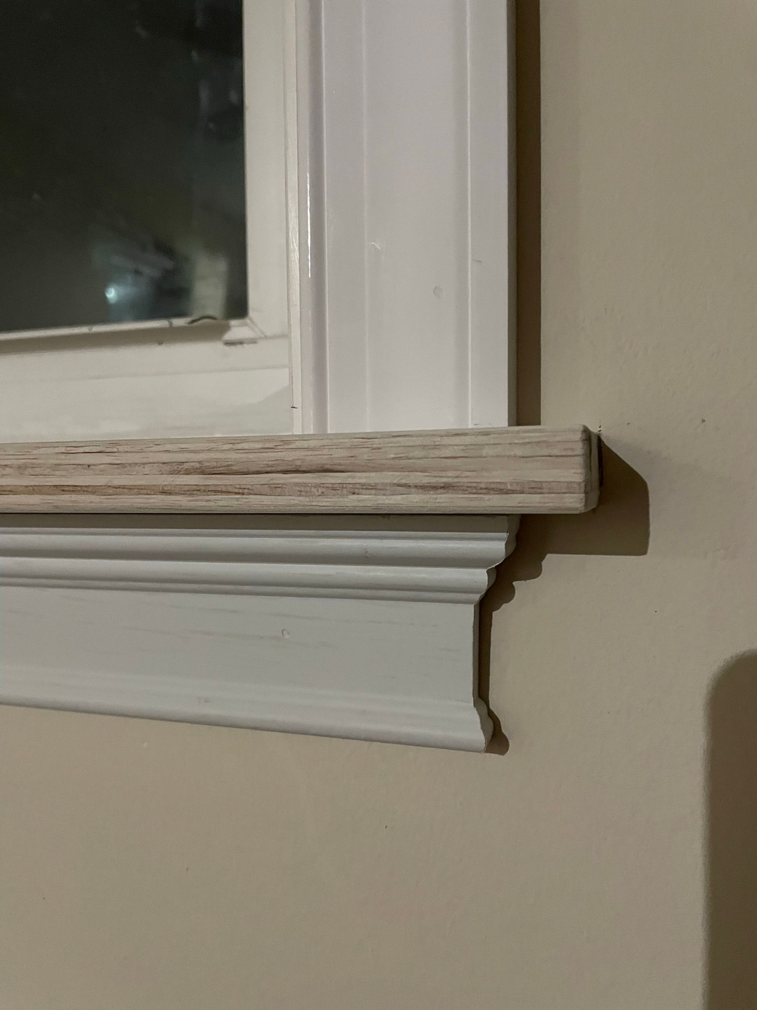 A window with a white trim and a wooden sill on a beige wall.