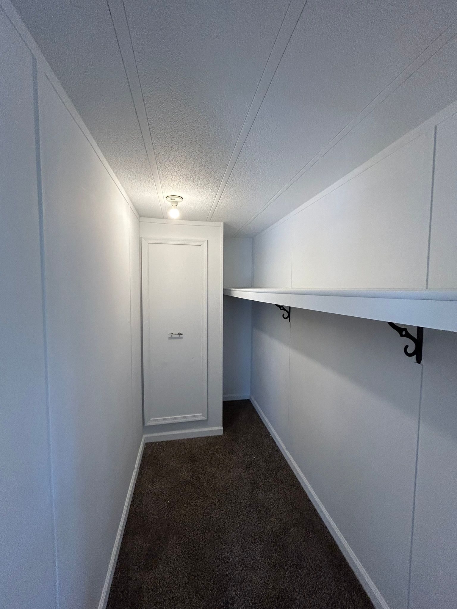 A long hallway with a shelf on the wall and a door.