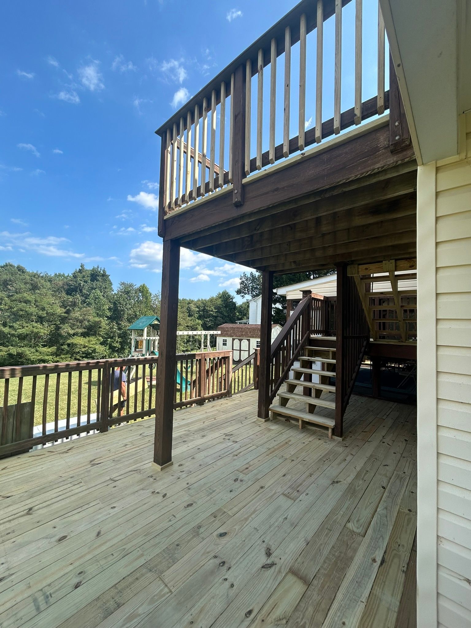 A wooden deck with stairs leading up to the second floor of a house.