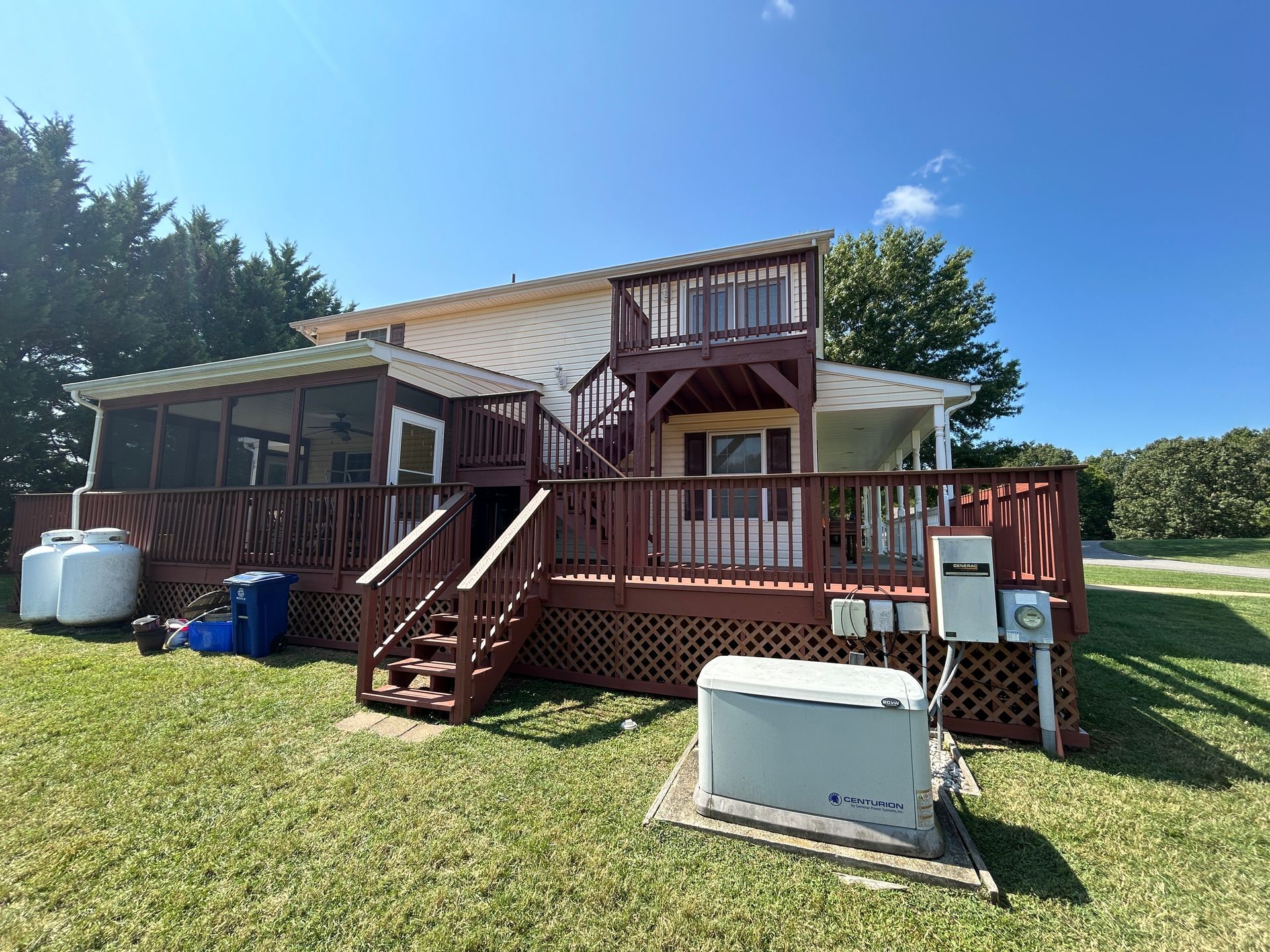 A house with a large deck and stairs is sitting on top of a lush green field.
