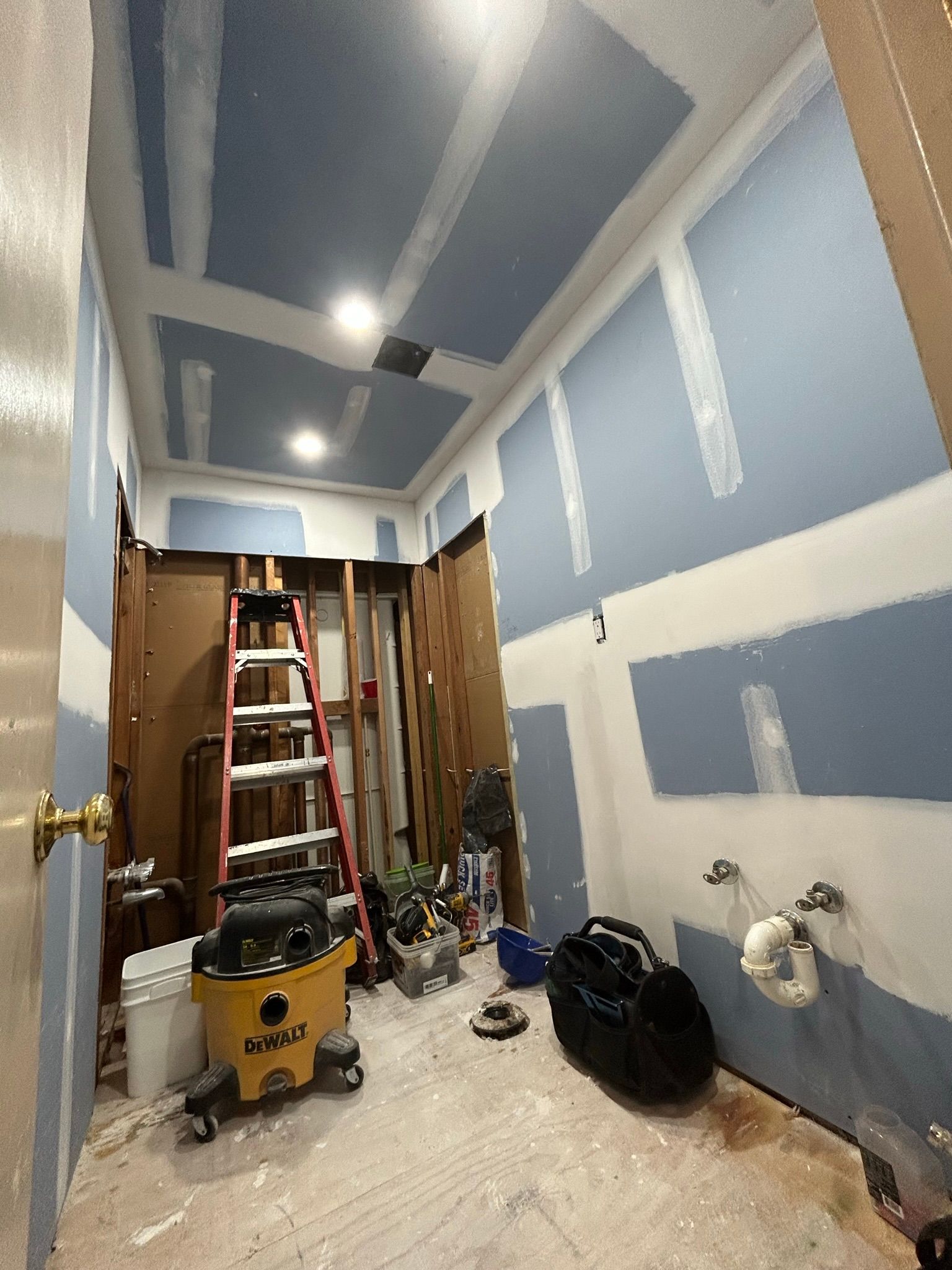 A bathroom under construction with a ladder and a vacuum cleaner.