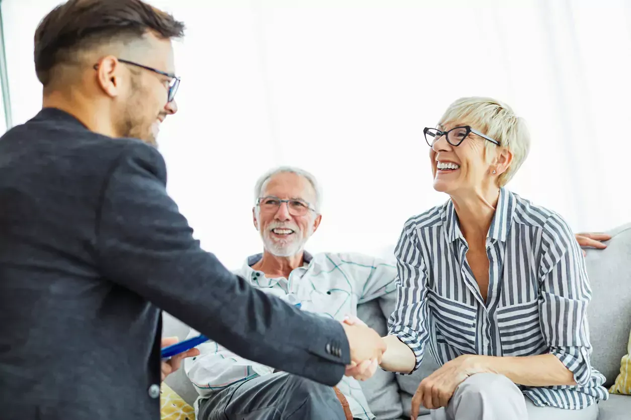 Man shaking hands with smiling woman as older couple watches, indoors.