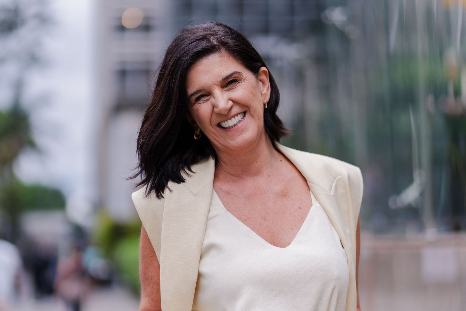 Smiling woman in a cream blazer outdoors against a blurred city background