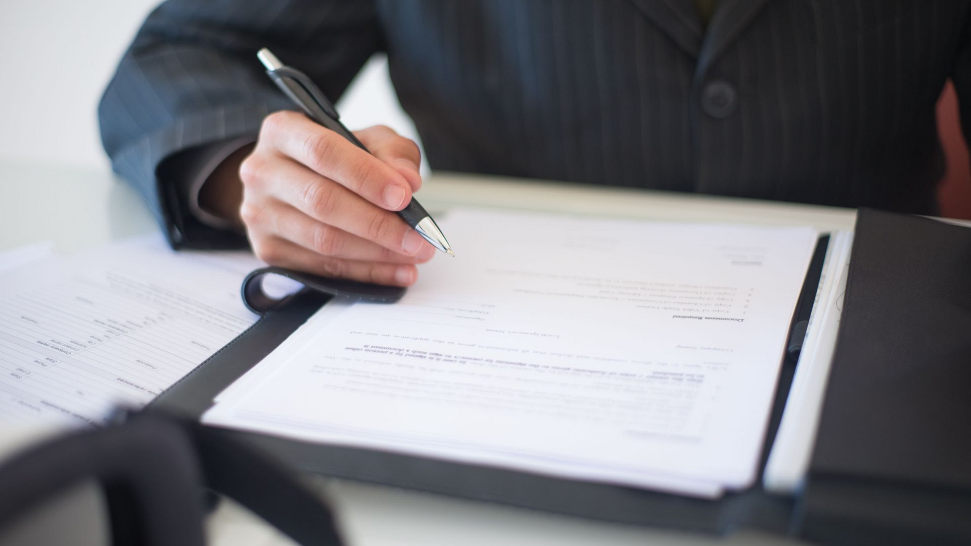 Hand signing a document on a clipboard with a pen
