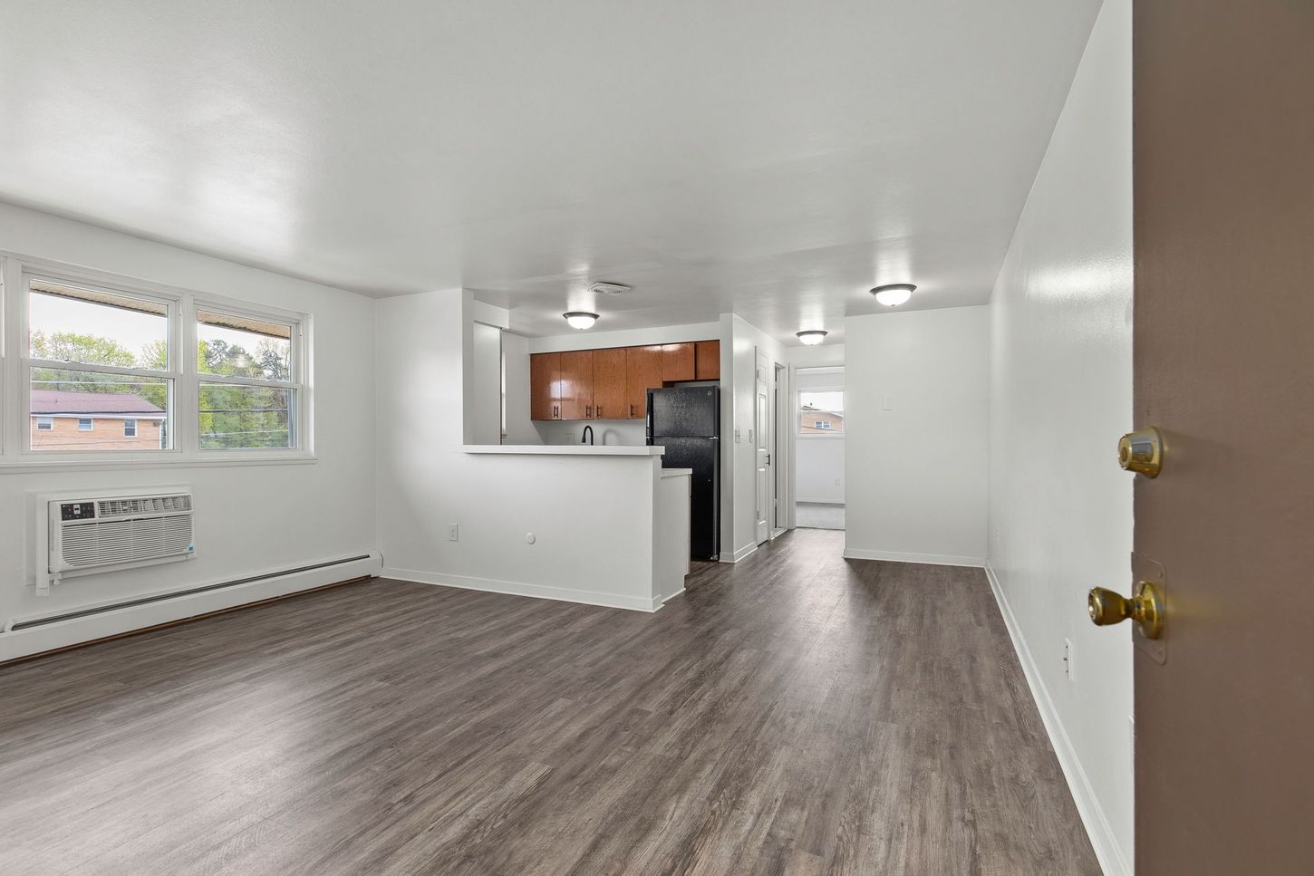 Apartment interior: living area with gray flooring, white walls, kitchen in the background.