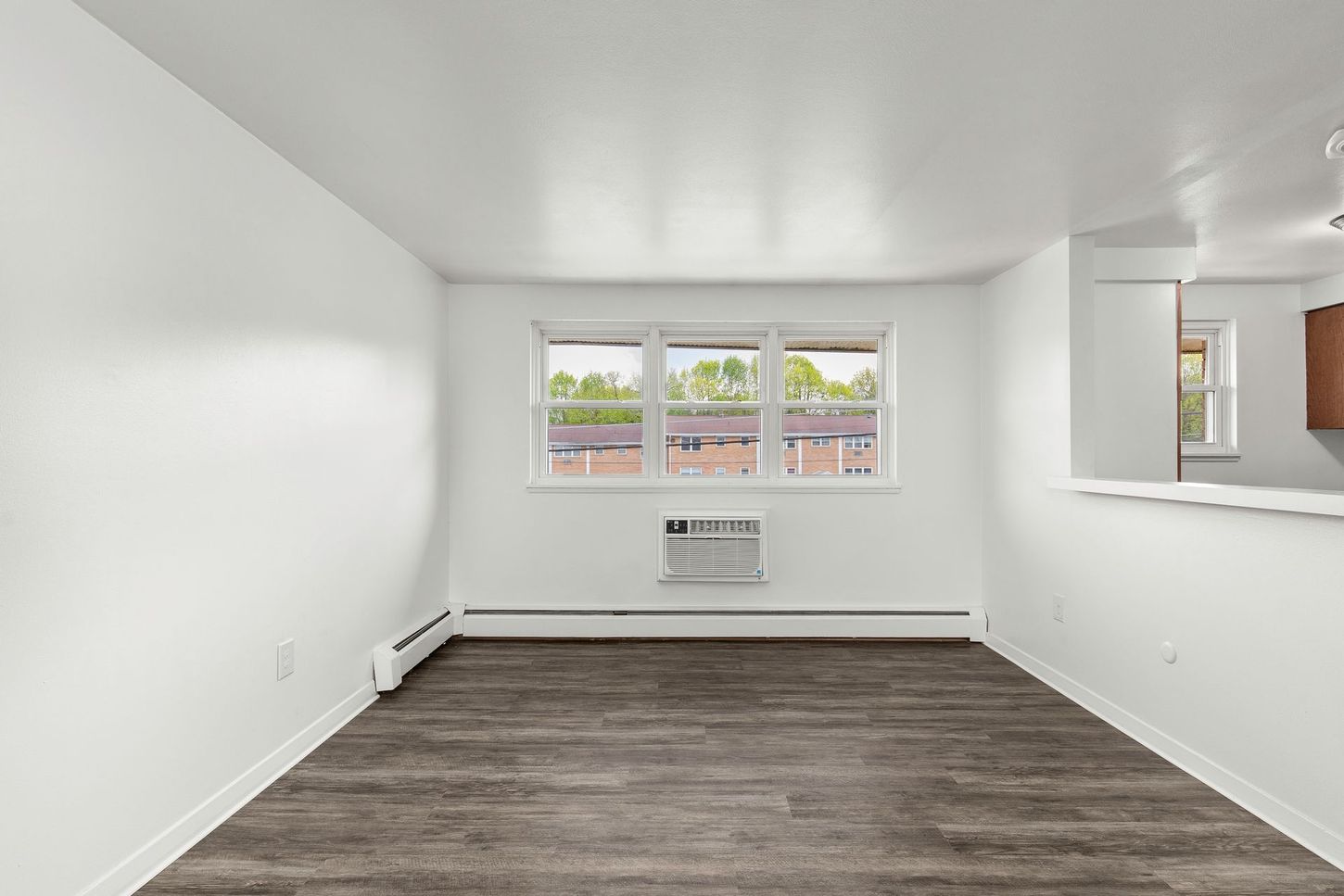 Empty apartment living room with a window, wood-look floor, and white walls.