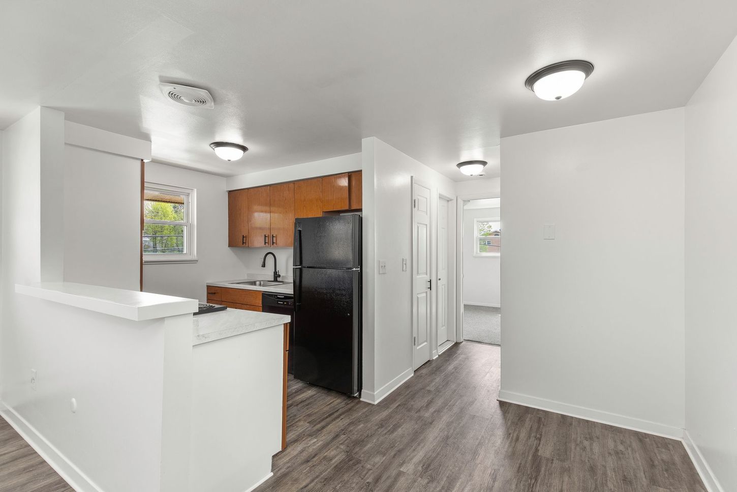 Kitchen area with dark appliances, wooden cabinets, and a hallway with white walls.