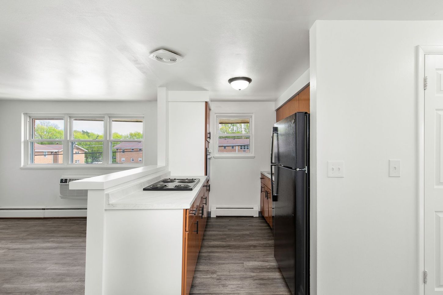 Kitchen with white countertops, dark refrigerator, and wood-toned cabinets; view of window and door.