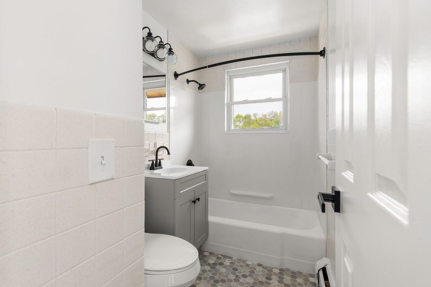 White bathroom with gray vanity, bathtub, and toilet. Black fixtures and hardware.