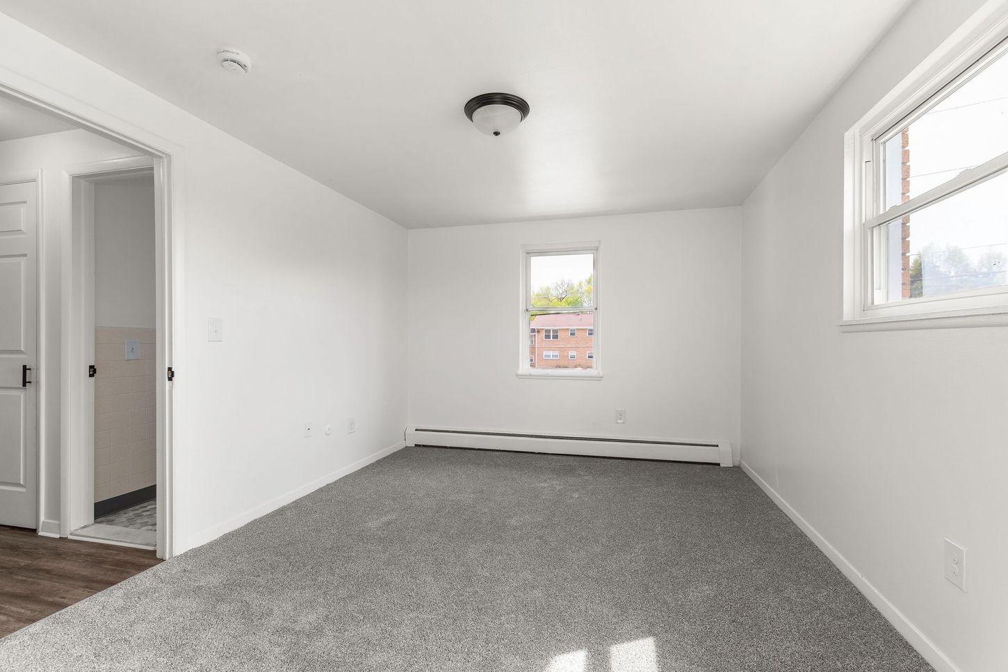 Empty bedroom with gray carpet, white walls, and a window.