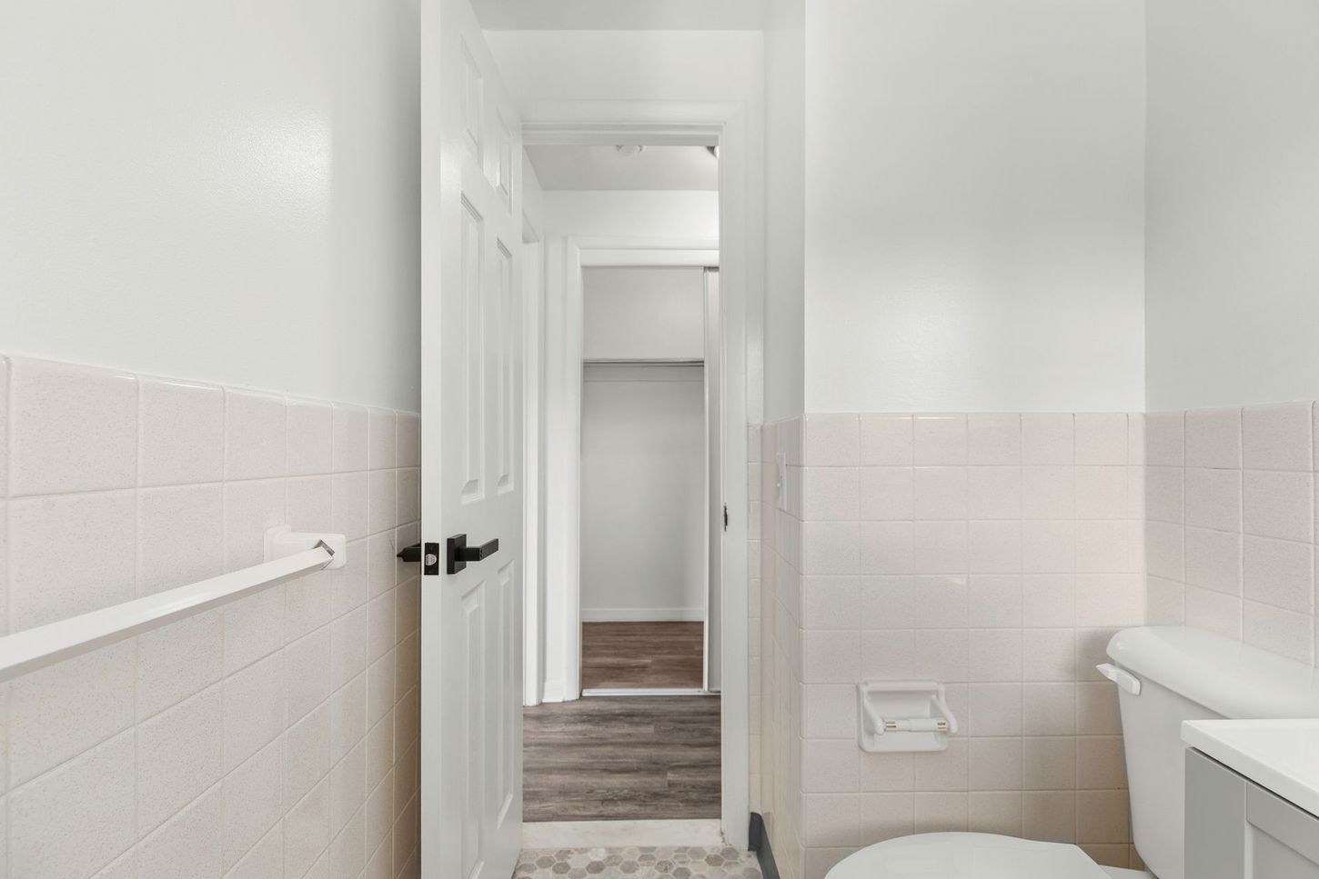 White bathroom with a toilet, door to hallway, and pink tiled wainscoting.