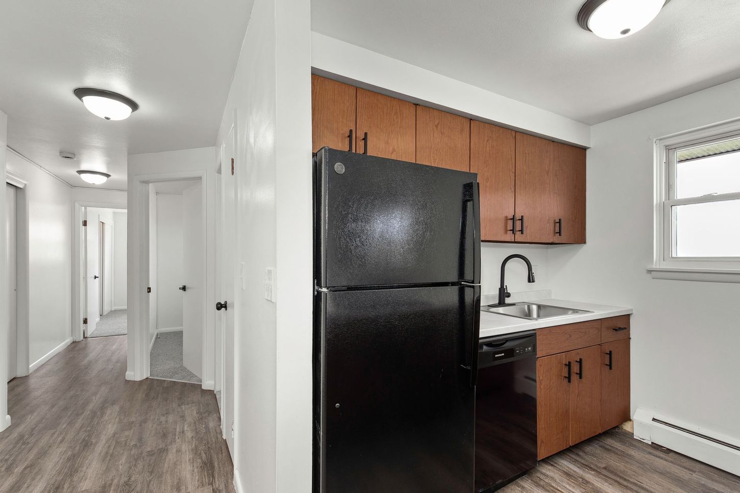Kitchen area with refrigerator, cabinetry, and hallway leading to rooms.