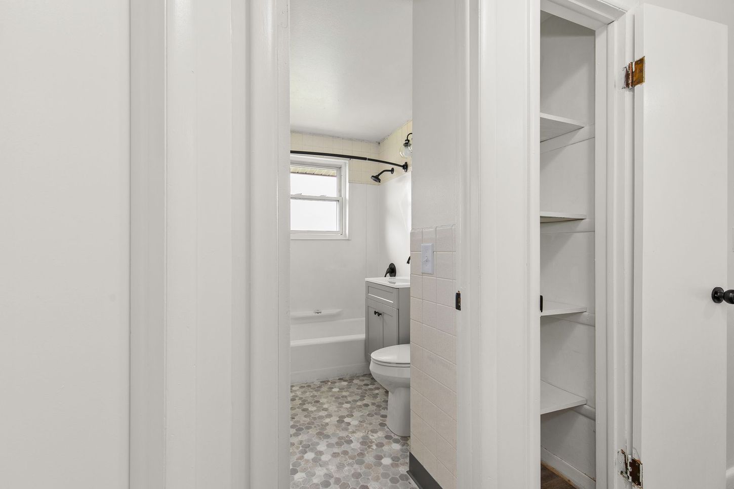 Bathroom doorway view; open white door reveals gray tiled floor, toilet, and shelves.