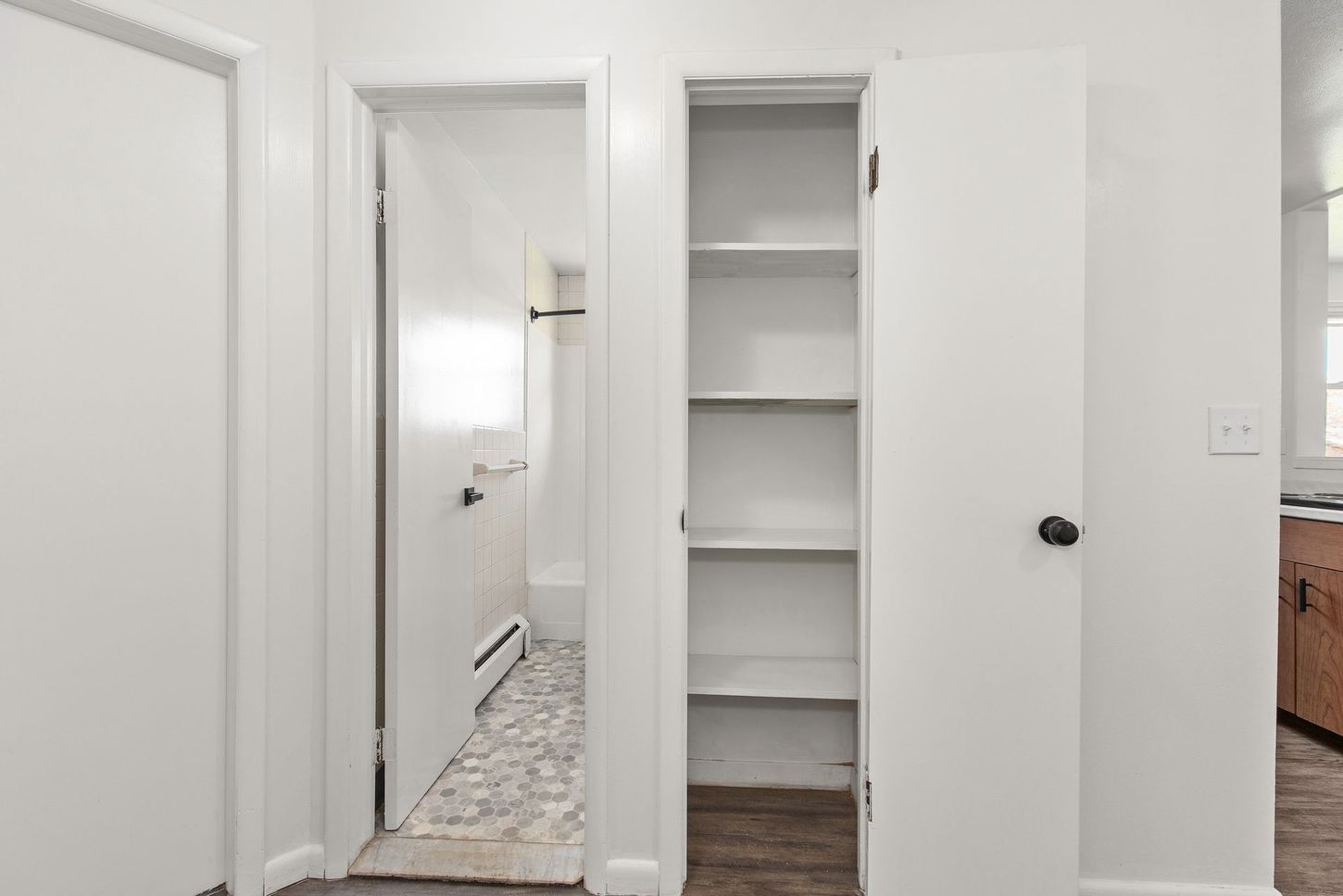 Hallway with open pantry, bathroom door ajar, and a closed white door.