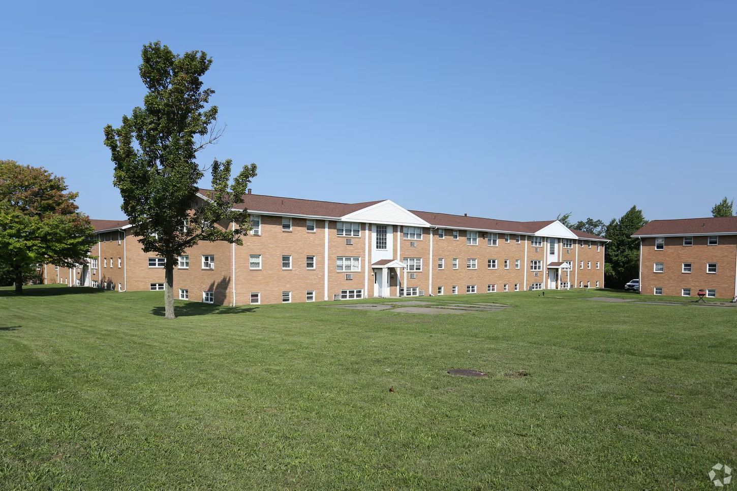 Large brick apartment complex with brown roof on a green lawn under blue sky.