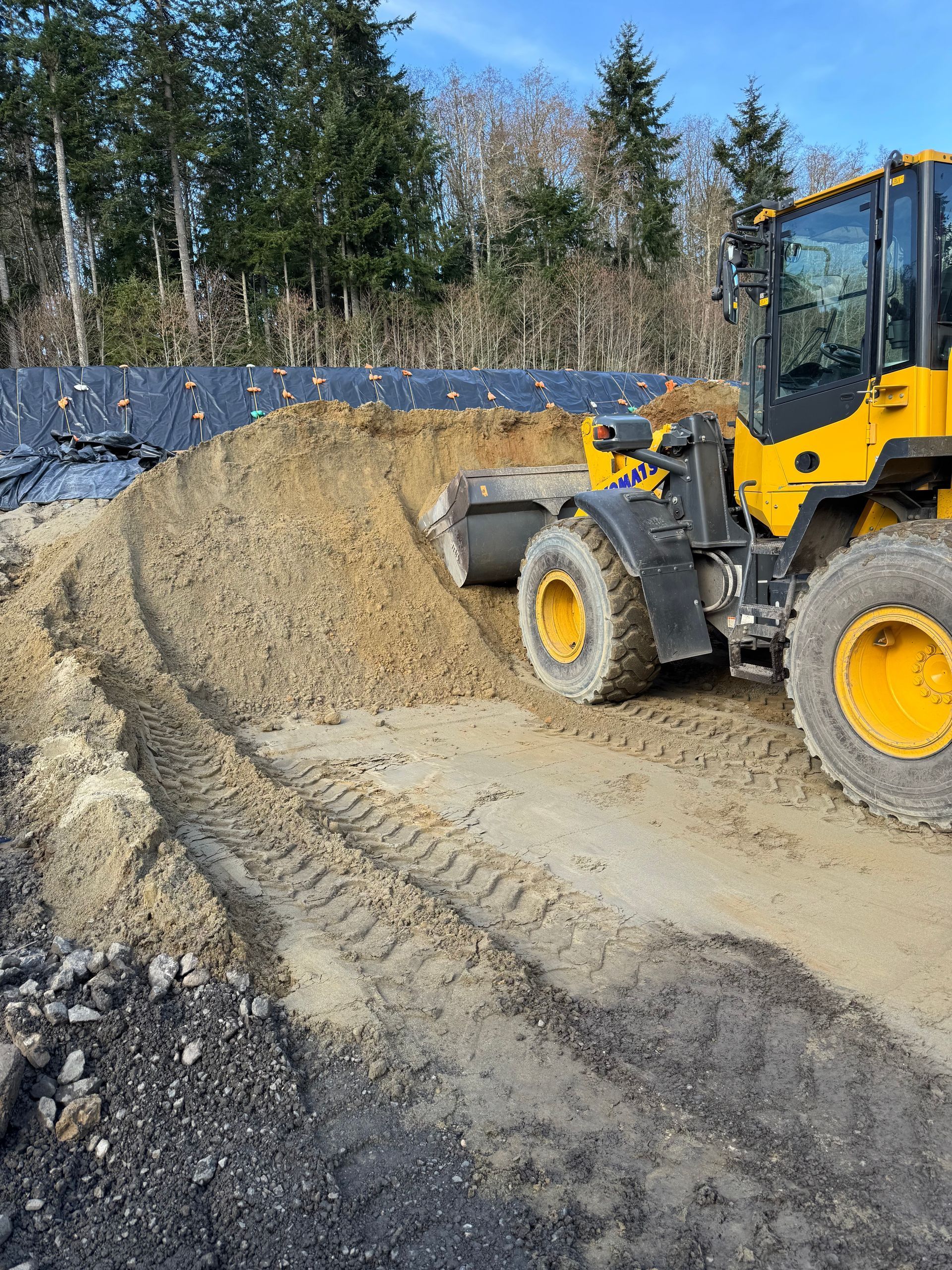 Yellow Komatsu loader scoops sand on a construction site.
