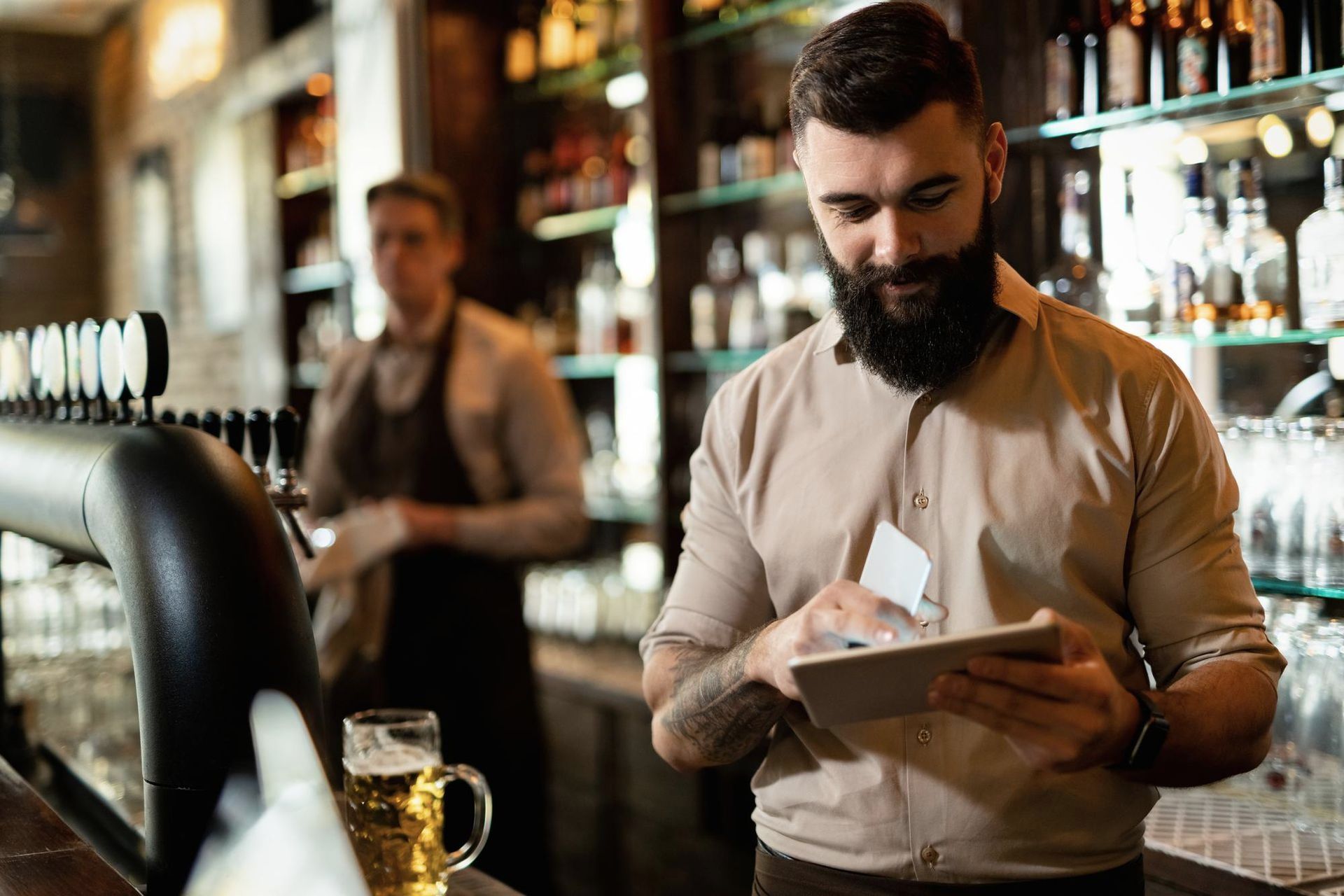 A man with a beard is using a tablet in a bar.