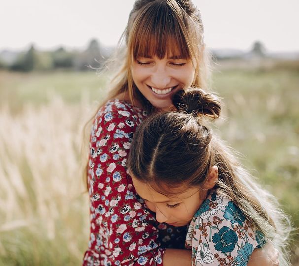 A woman is hugging a little girl in a field.