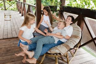 A woman and three children are sitting in a chair on a porch.