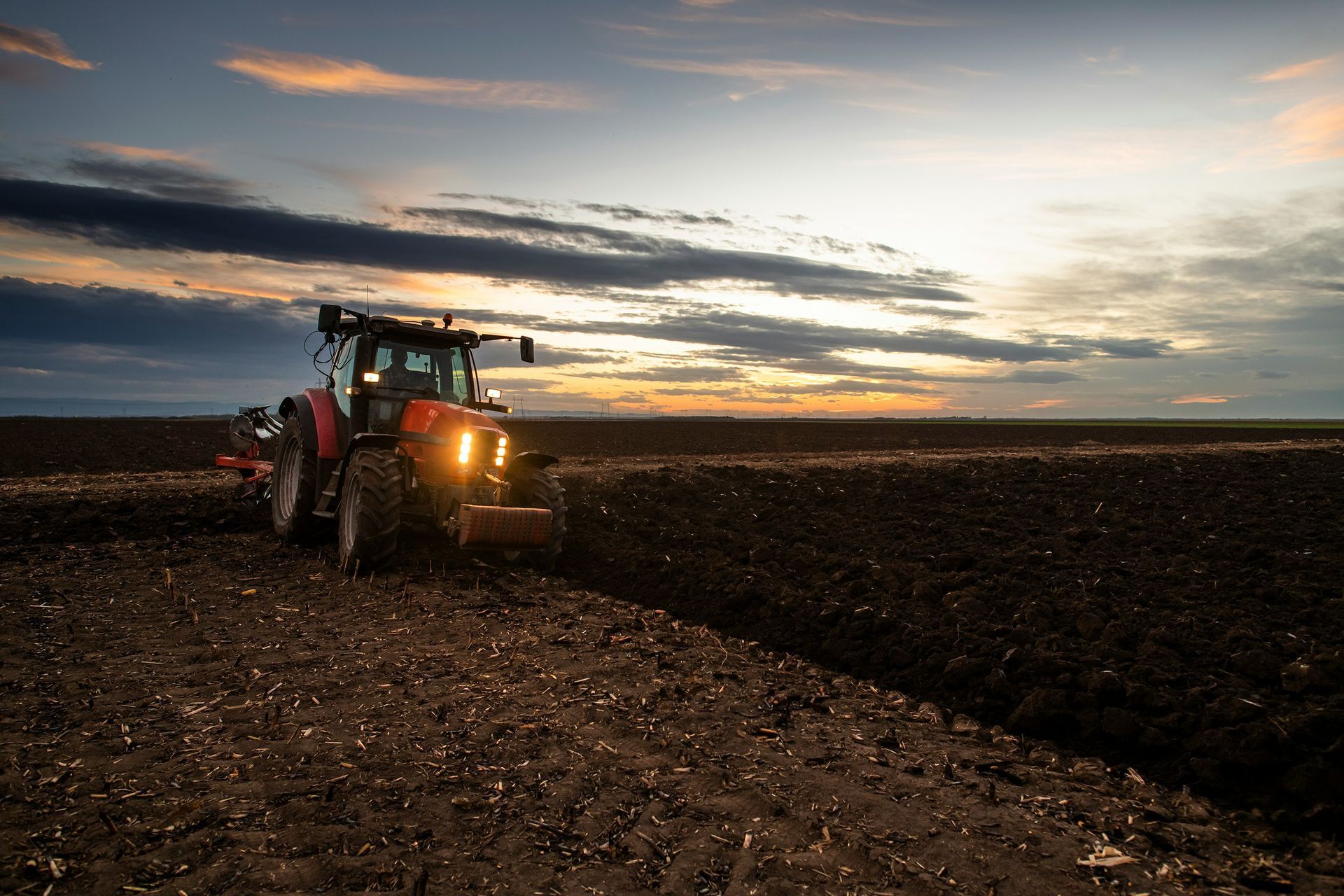 A tractor is plowing a field at sunset. 