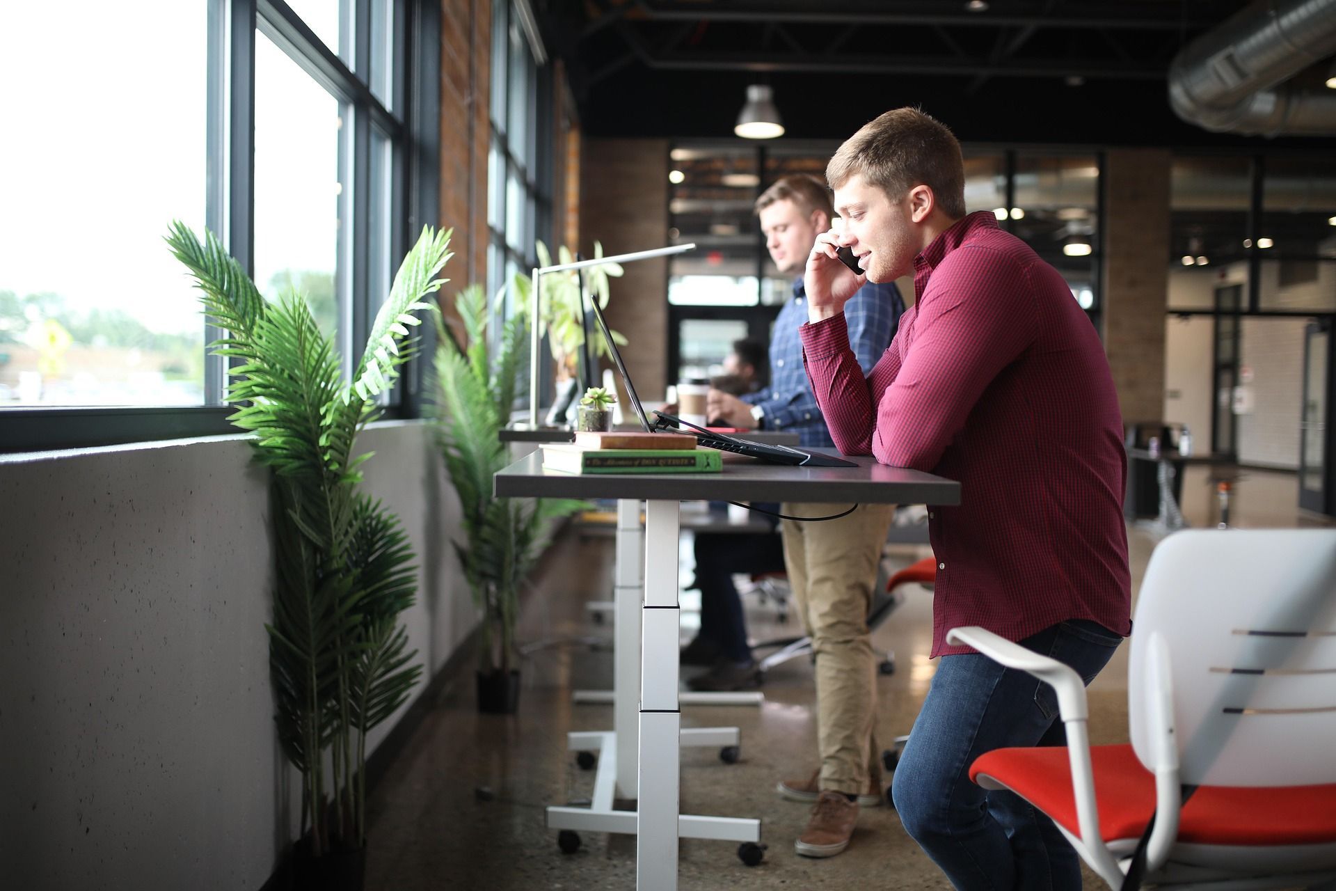 A man is sitting at a standing desk talking on a cell phone.