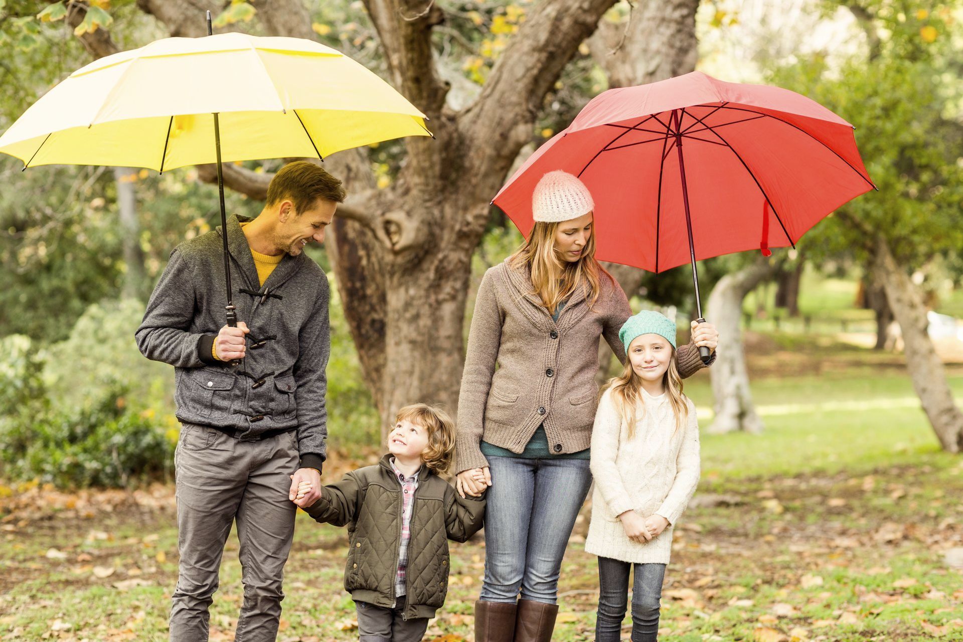 A family is holding hands under umbrellas in a park.