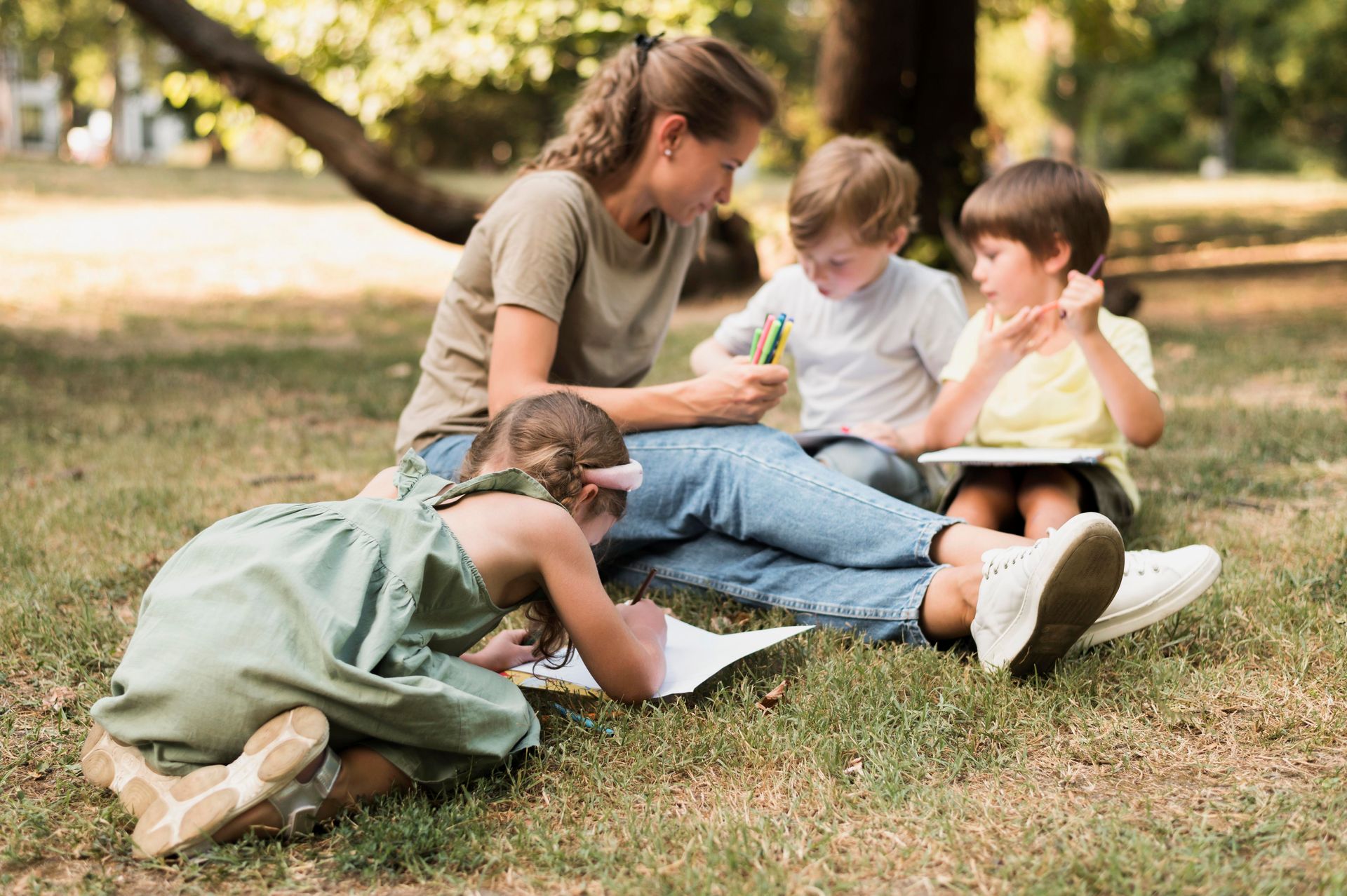 A woman is sitting on the grass with three children.