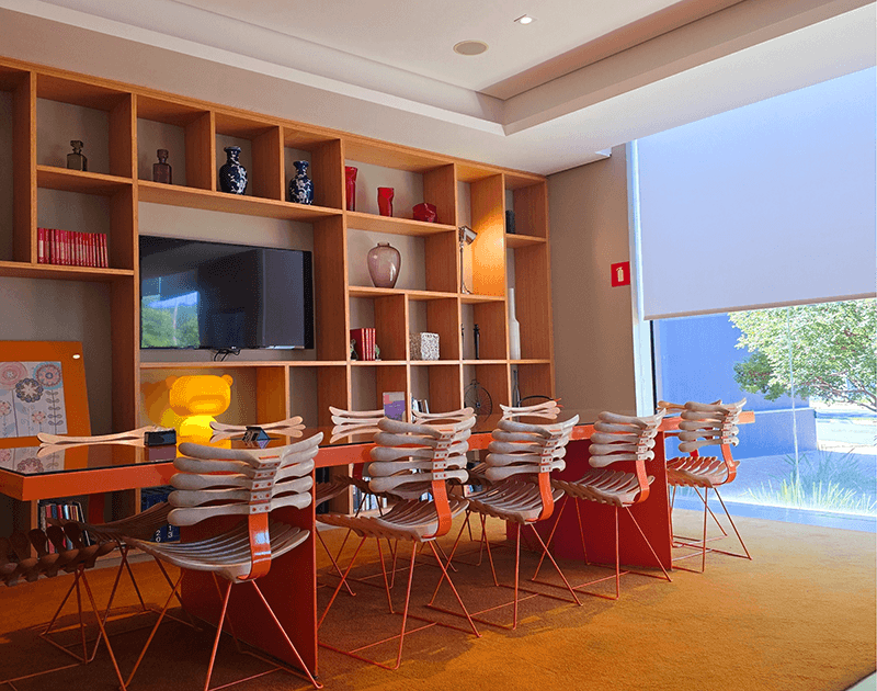 Sala de conferências moderna com uma longa mesa laranja, cadeiras esculturais exclusivas e estantes de madeira que vão do chão ao teto.