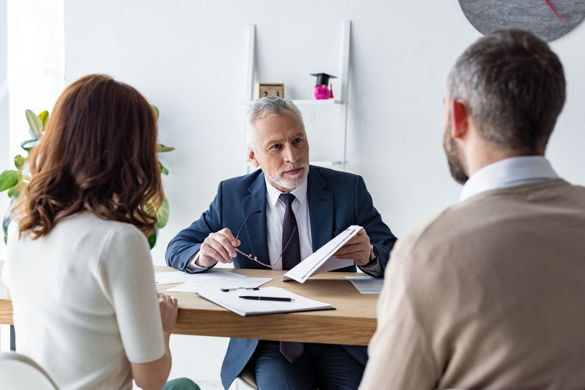 A man in a suit and tie is sitting at a table talking to a couple.