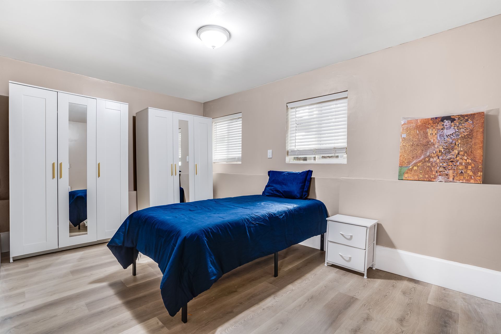 A bedroom with a single bed , white cabinets , a nightstand , and a painting on the wall.