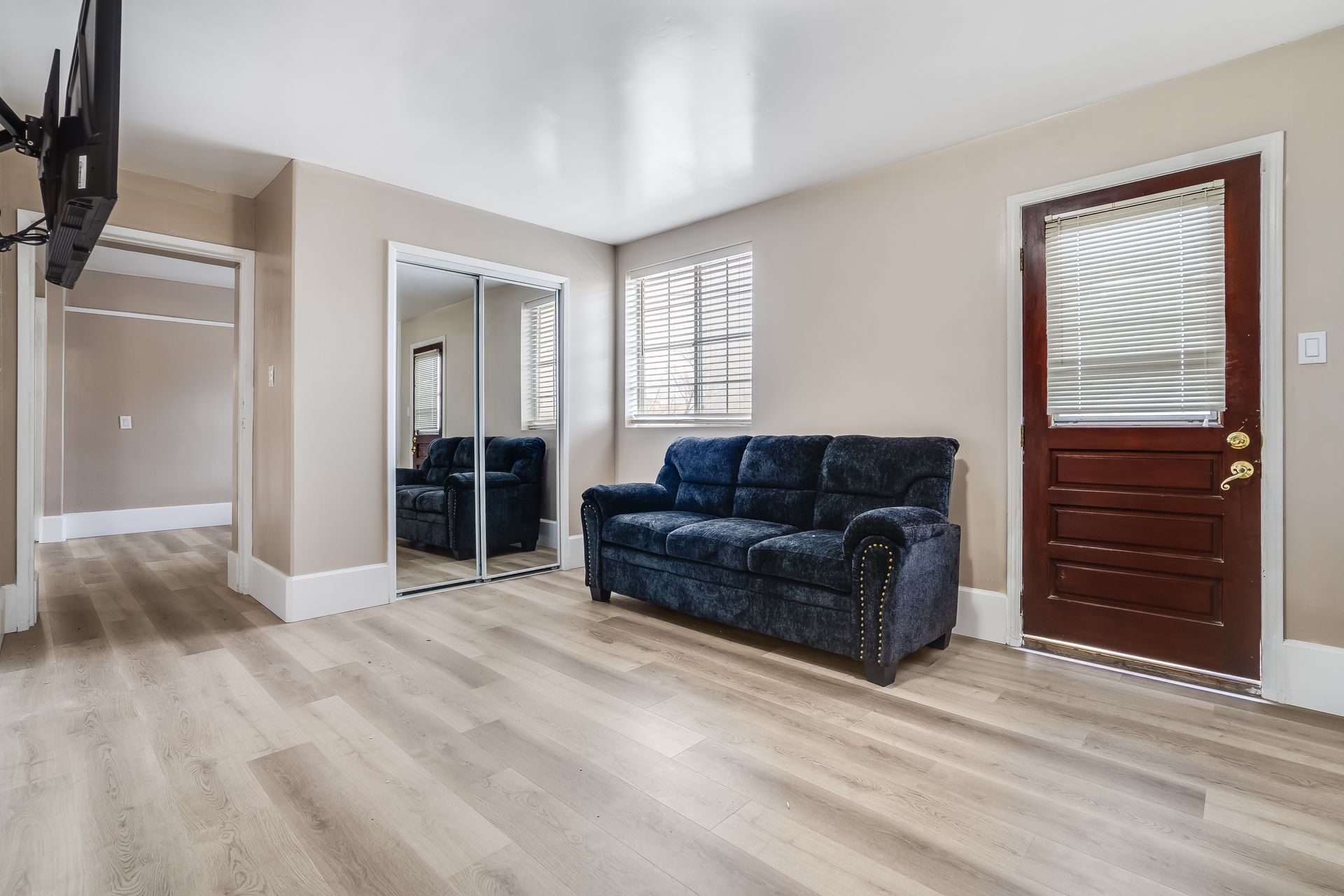 A living room with hardwood floors , a couch , a television and a door.