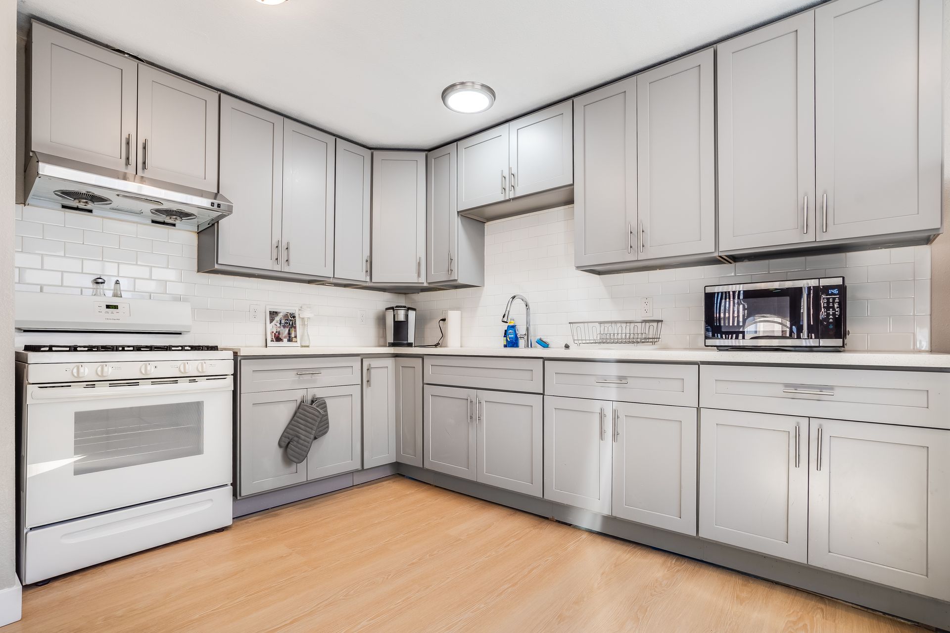 A kitchen with white cabinets , a stove , a microwave , and a sink.