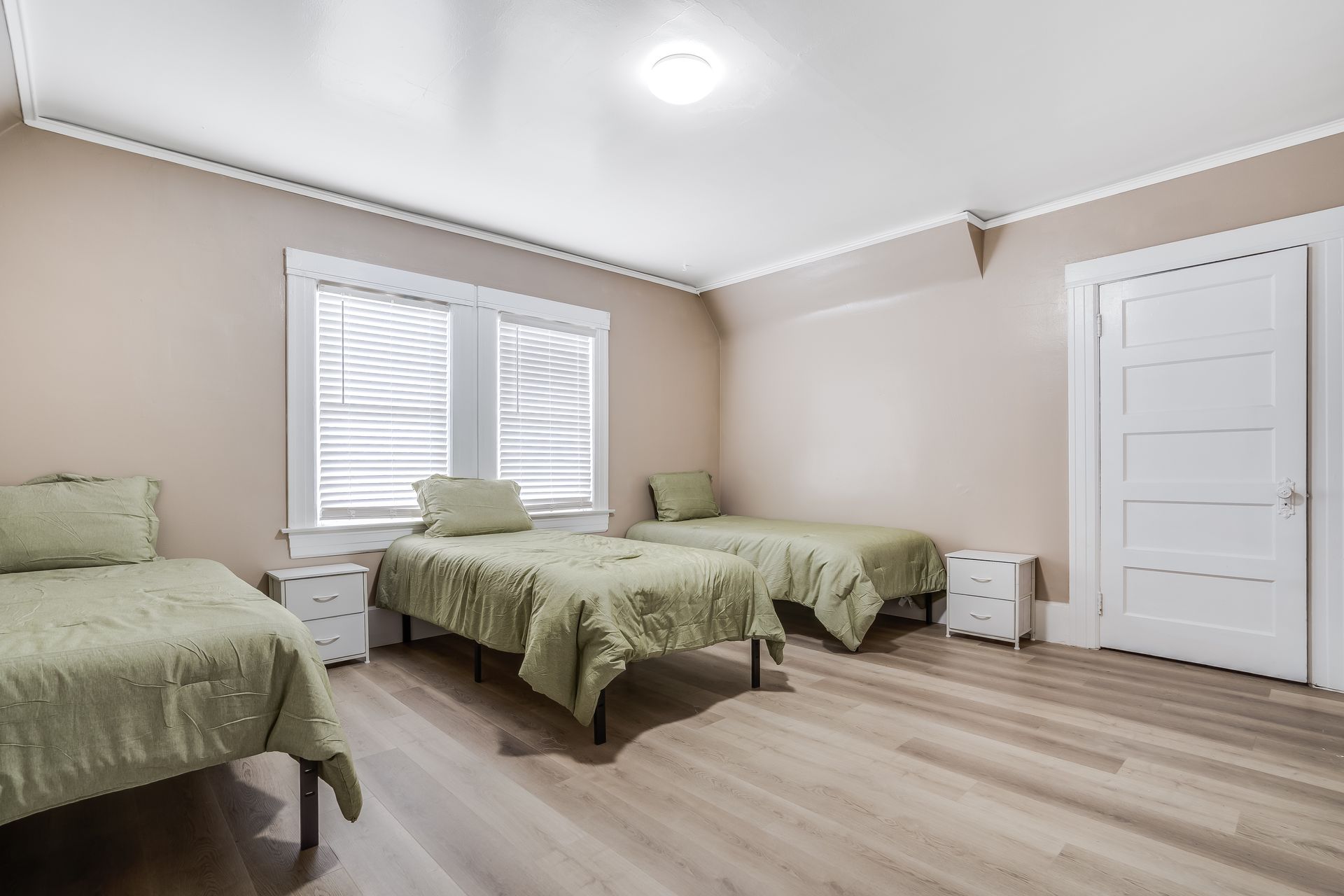 A bedroom with three beds , two nightstands , and two windows.