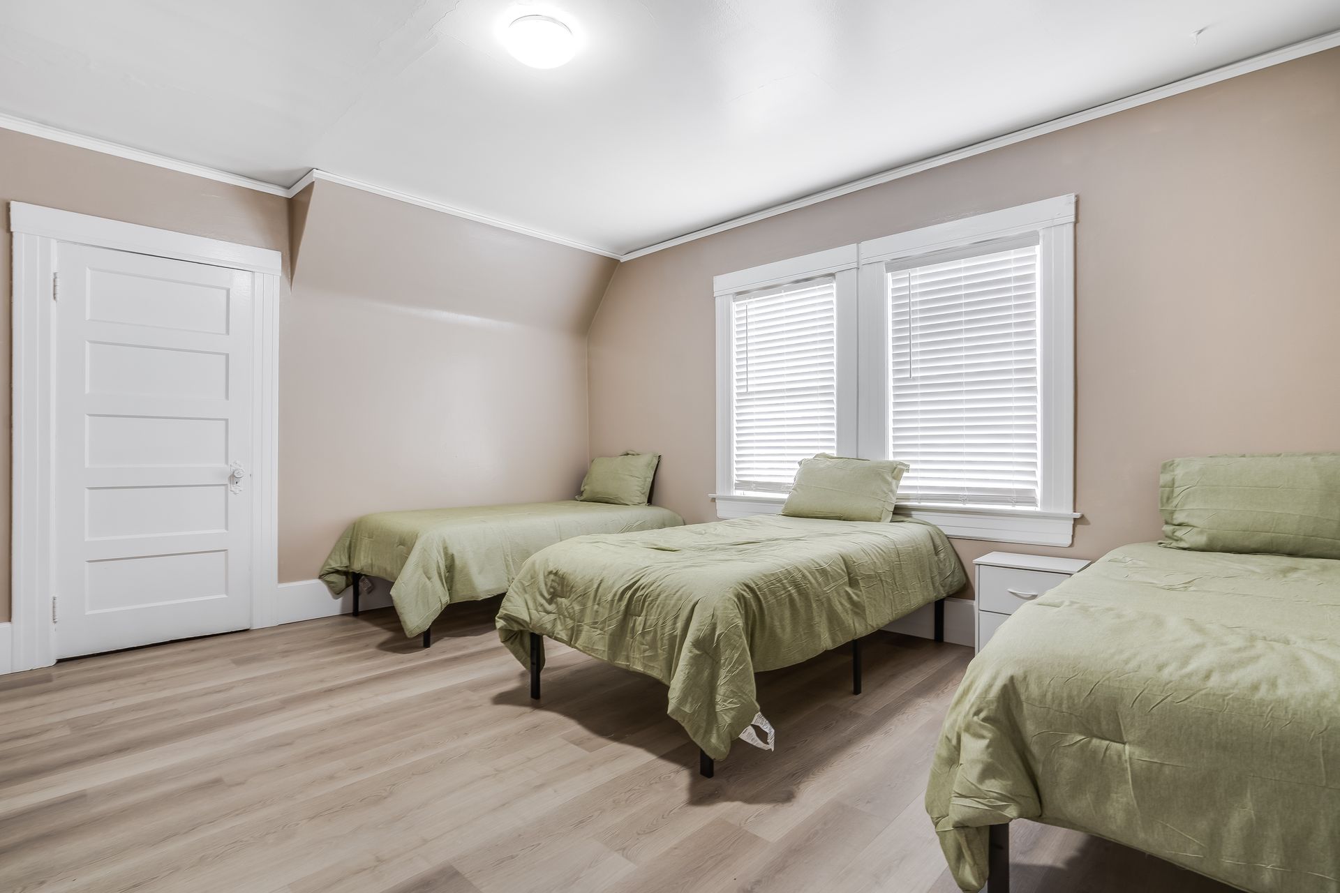 A bedroom with three beds and two windows.