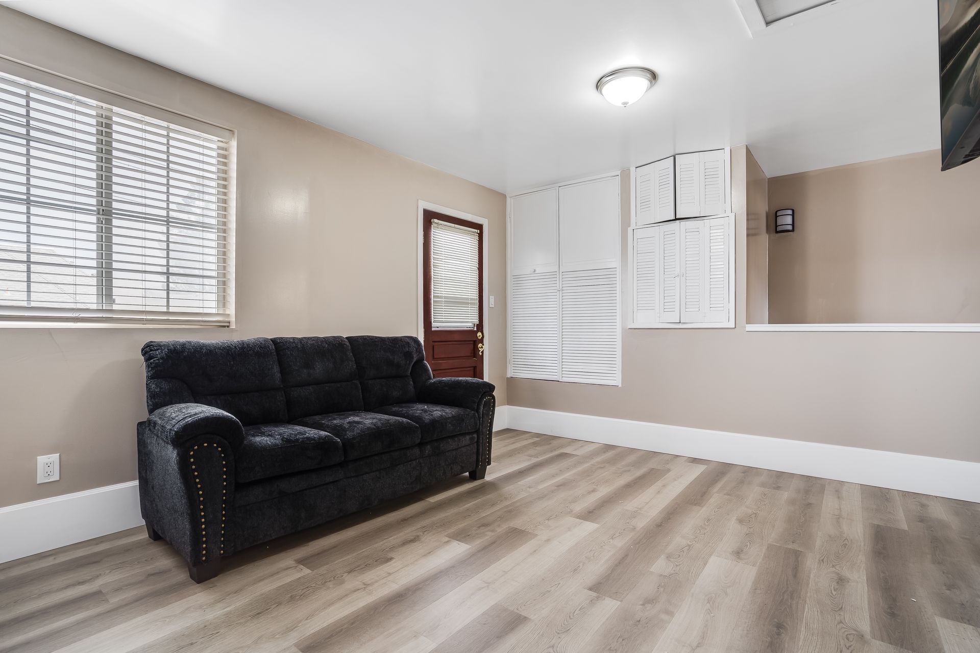 A living room with a black couch and hardwood floors.