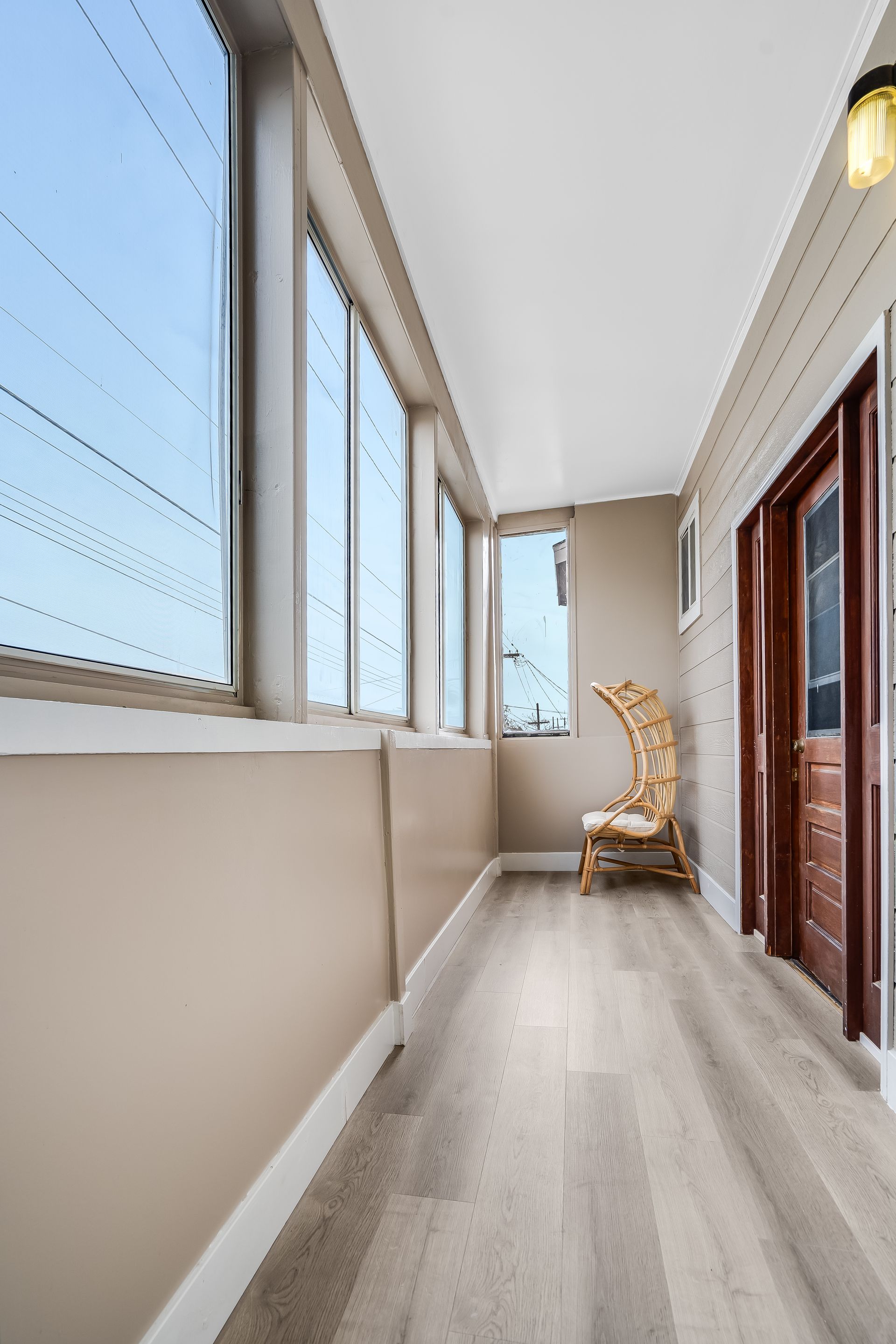 A long hallway with a wicker chair and lots of windows.