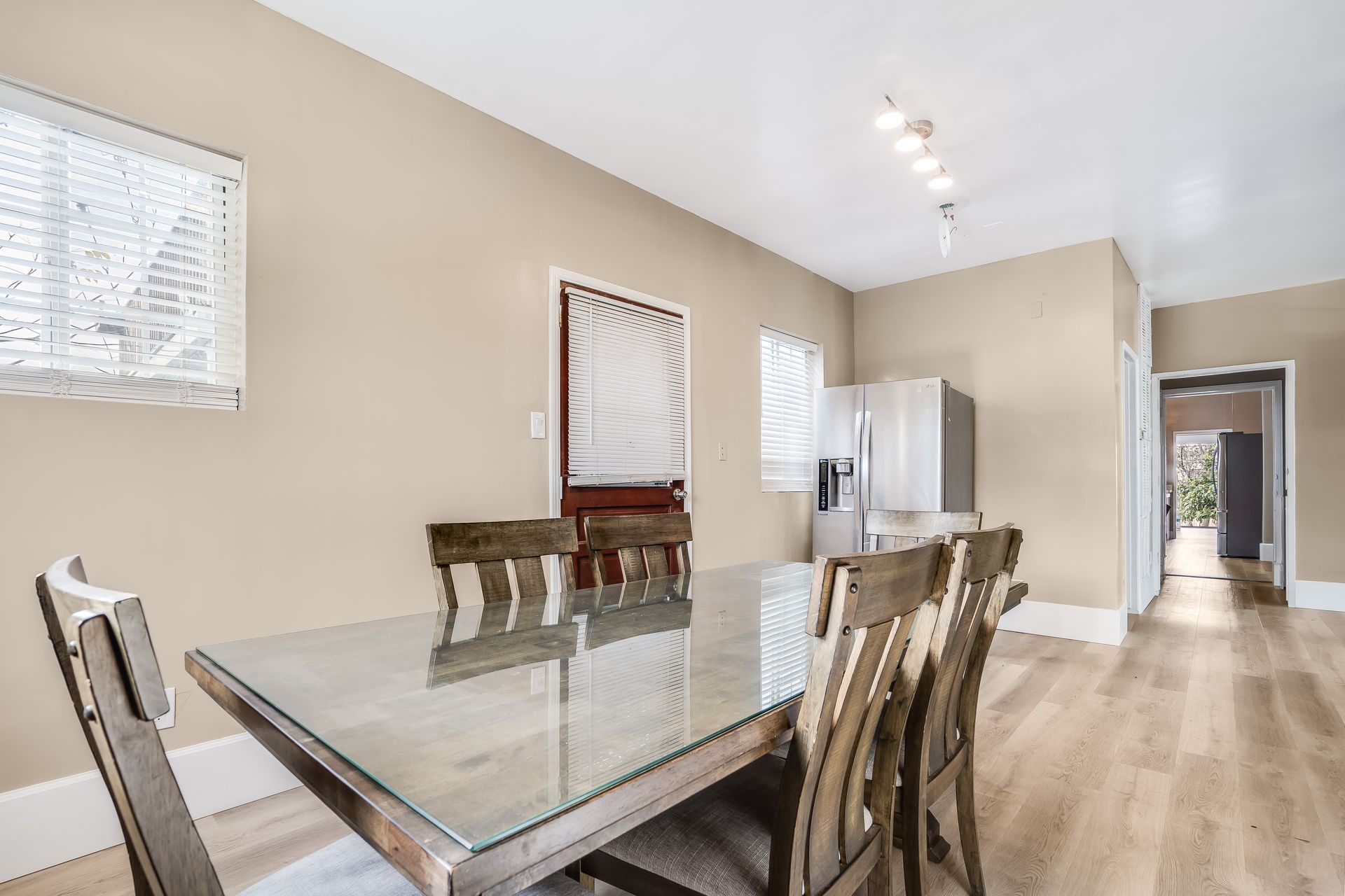 A dining room with a glass table and chairs and a refrigerator.