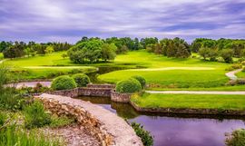 Lush green golf course with a winding stone path, pond, and trees under a purple sky