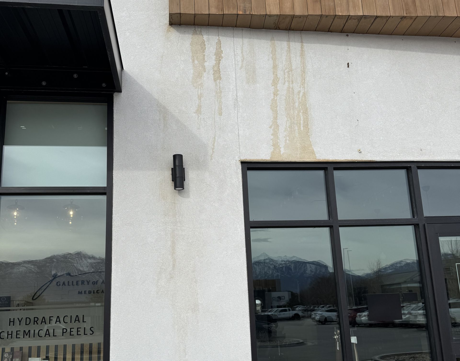Stucco building facade showing vertical rust-colored water staining beneath a wood accent panel and above window frames.
