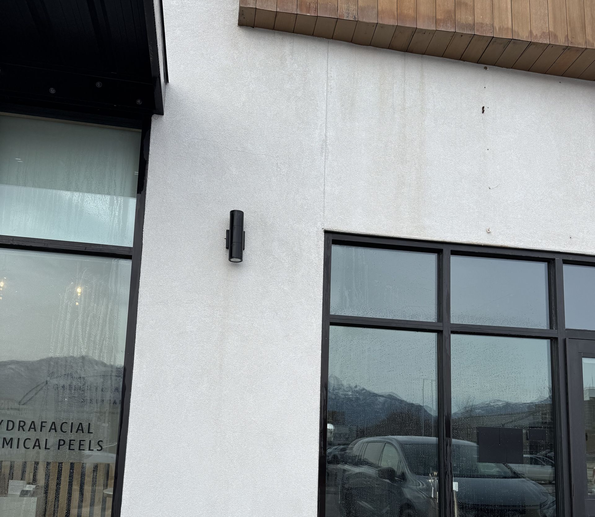 A storefront exterior with white textured stucco walls, black window frames, and a vertical light fixture.