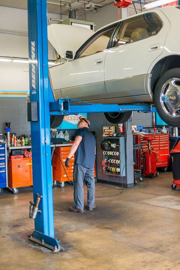 A man is standing next to a car on a lift in a garage. | The Garage in Renton