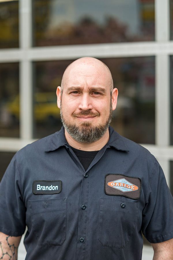 A man with a beard and a name tag on his shirt is standing in front of a garage door. | The Garage in Renton