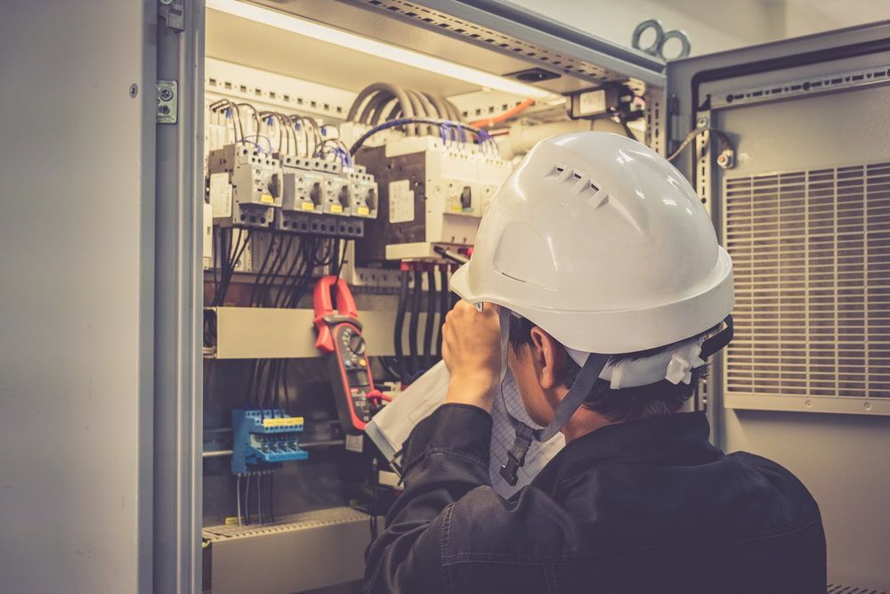 A Man Wearing a Hard Hat is Working on an Electrical Box — Aurablue Electric in Newcastle, NSW