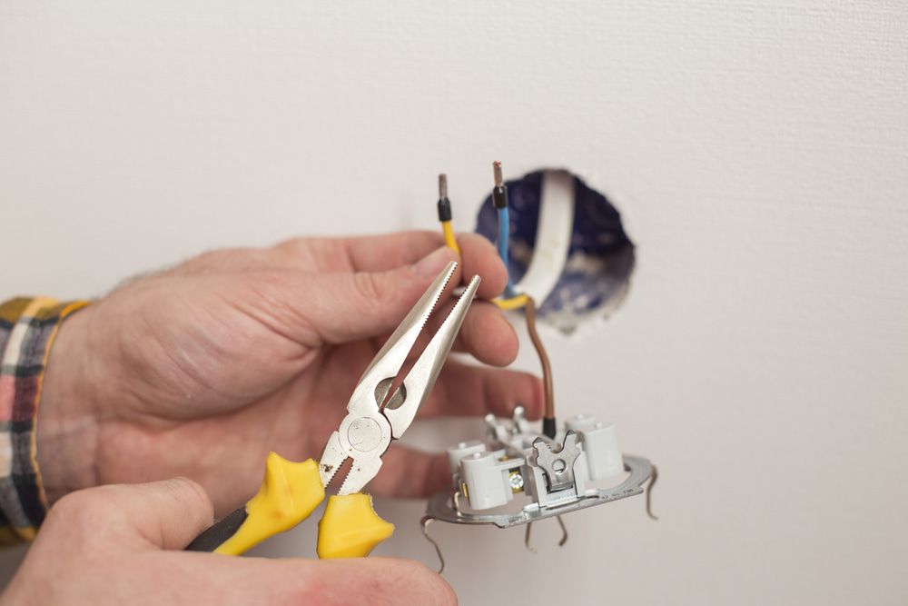 A Person is Fixing a Light Switch With Pliers — Aurablue Electric in Maitland, NSW