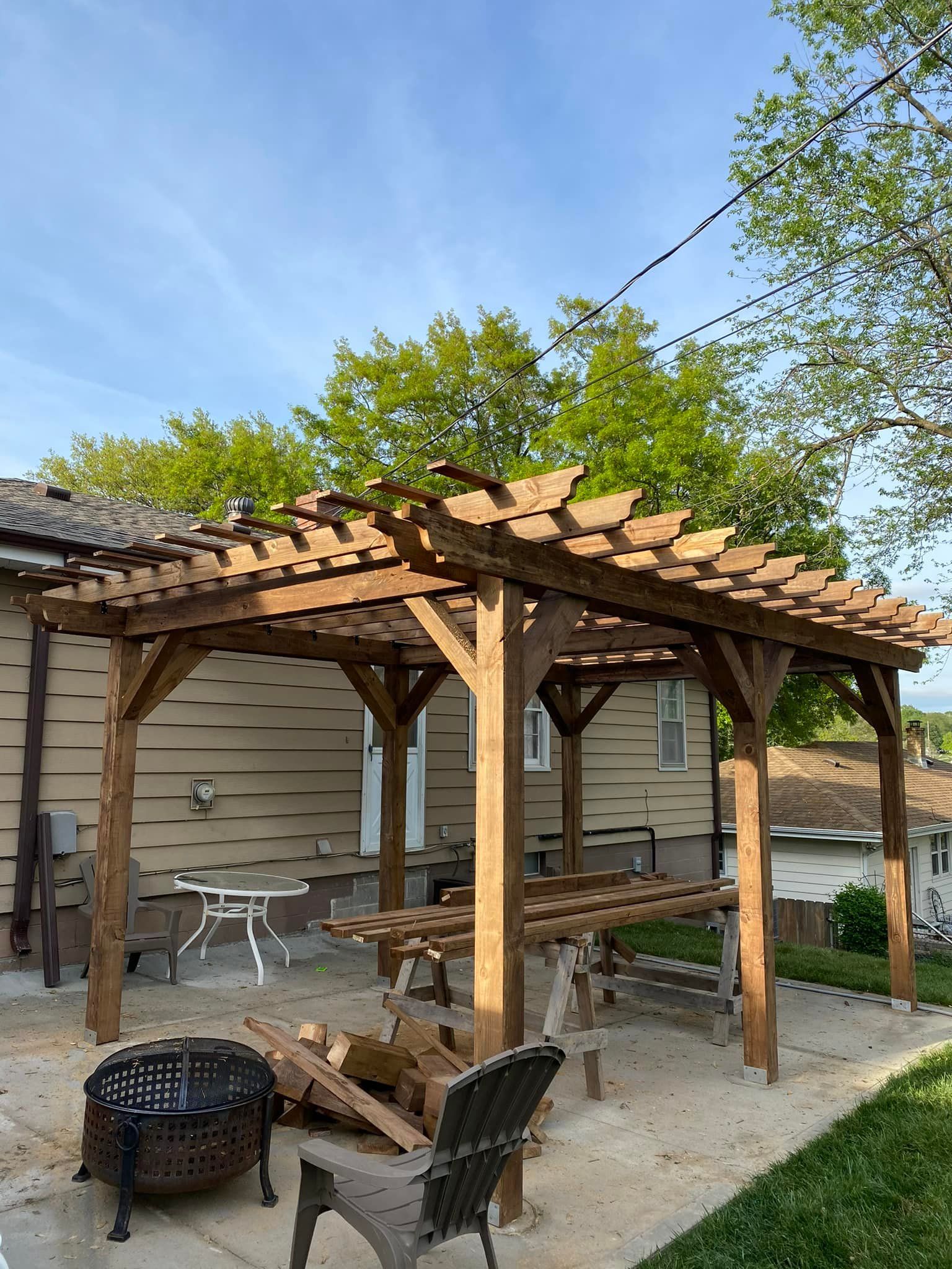 A wooden pergola with a fire pit in front of a house.