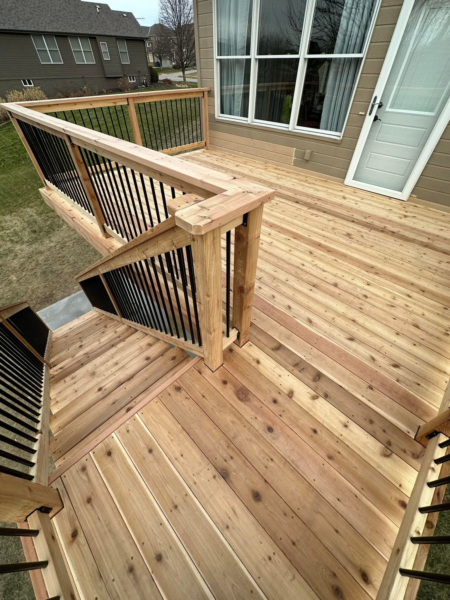 A wooden deck with stairs and railing in front of a house.