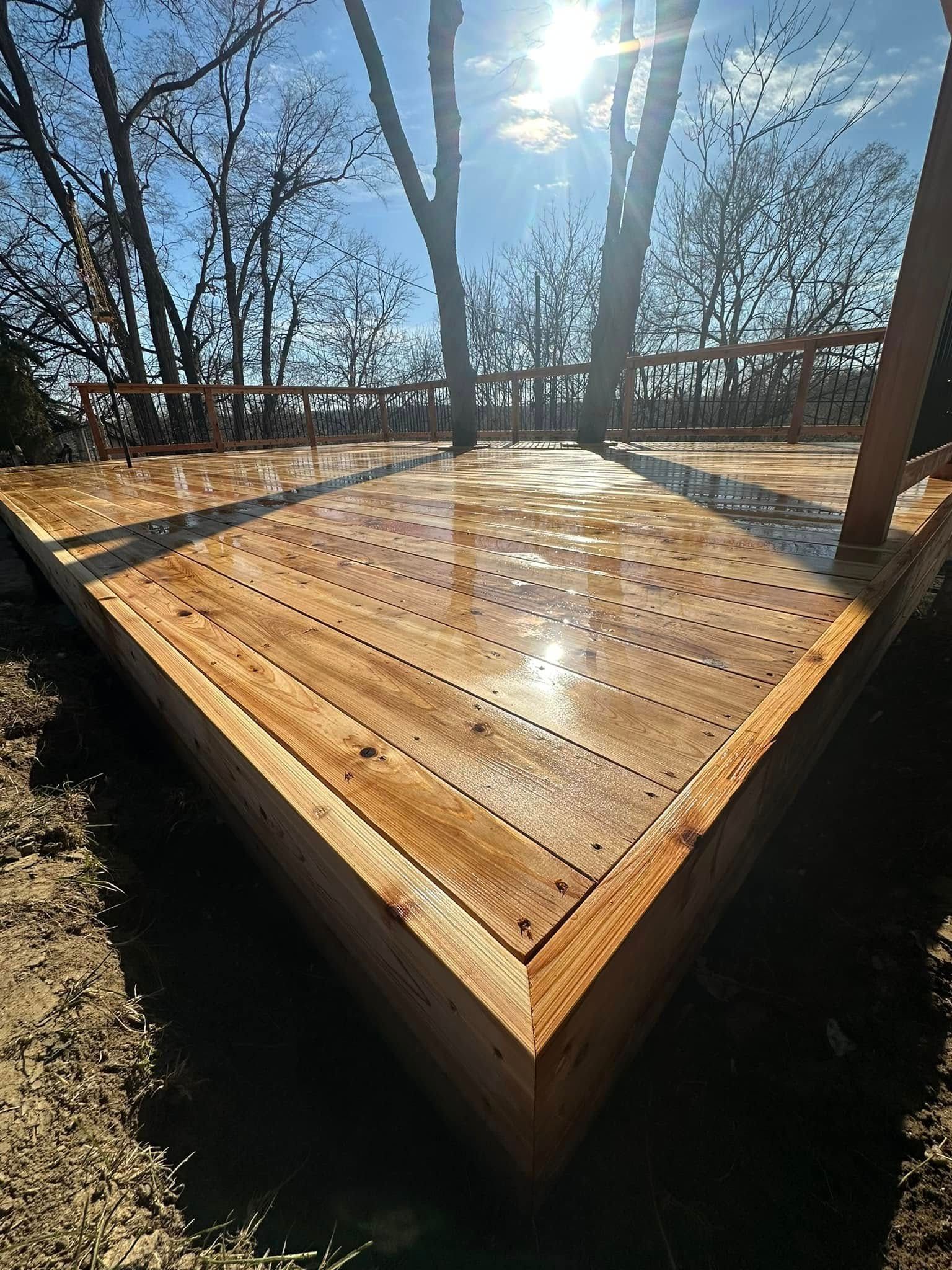 A wooden deck with trees in the background and the sun shining through the trees.