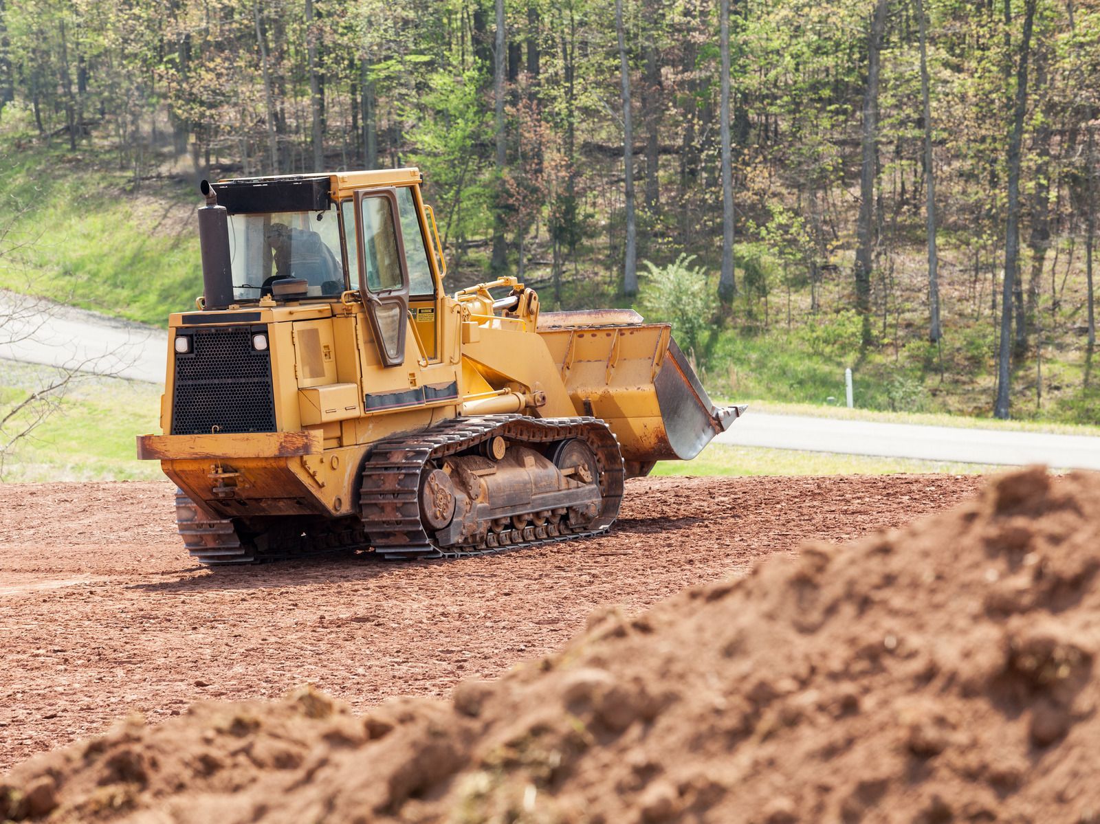 Yellow skid steer moving dirt at a construction site near a building.