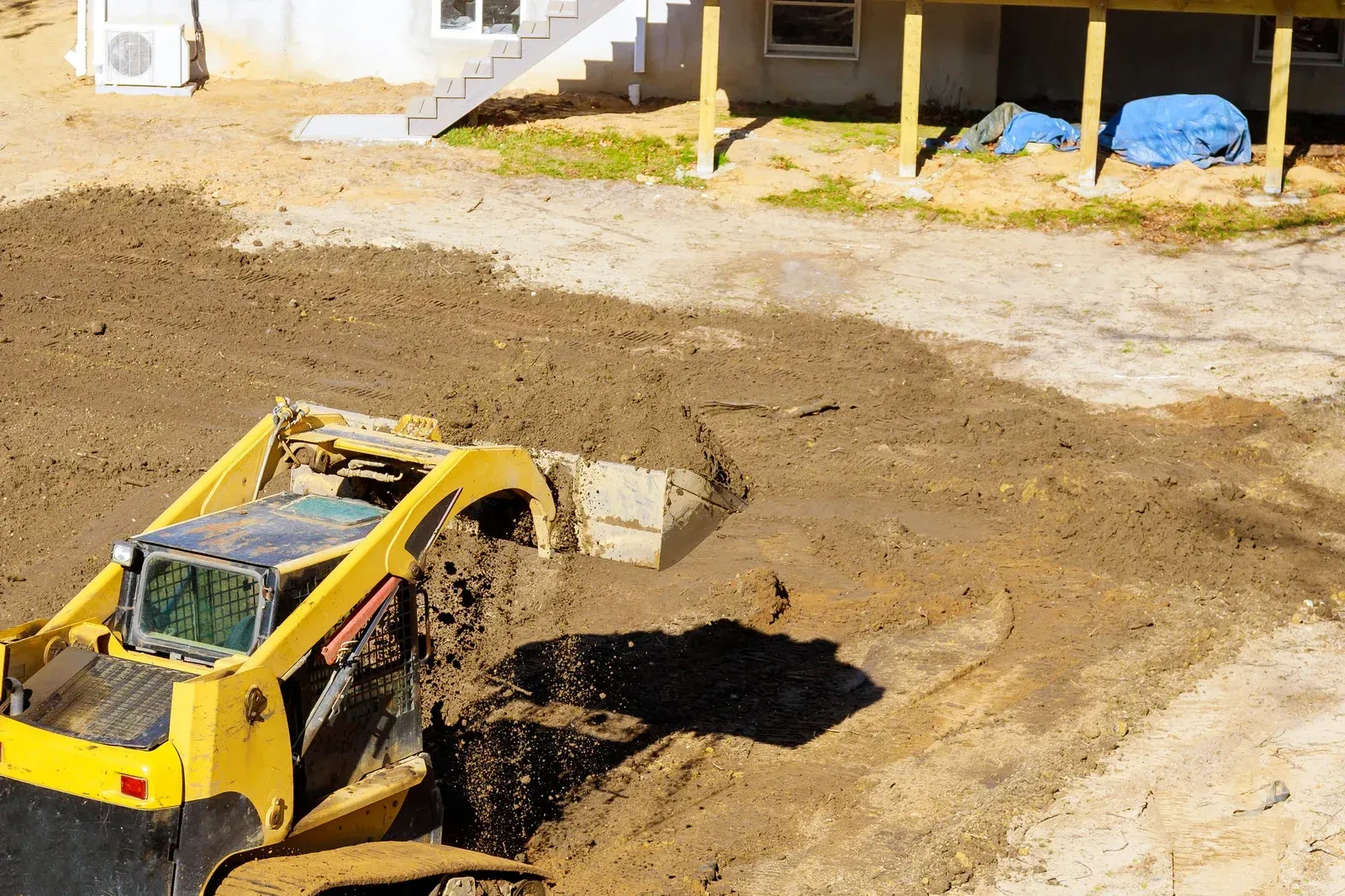 Yellow skid steer moving dirt near a building under construction.