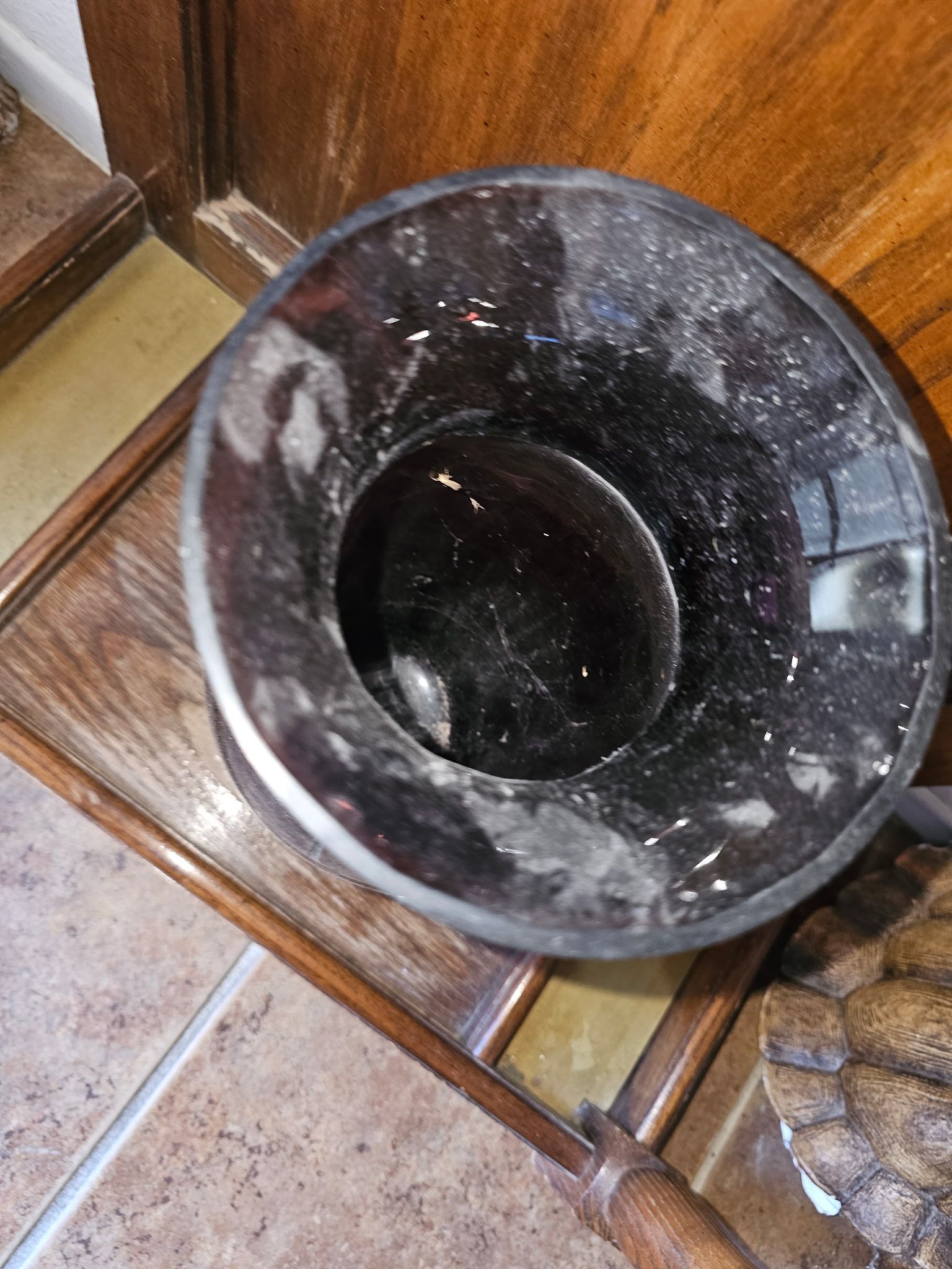 Black trash can on a wooden table, sitting on a tile floor.